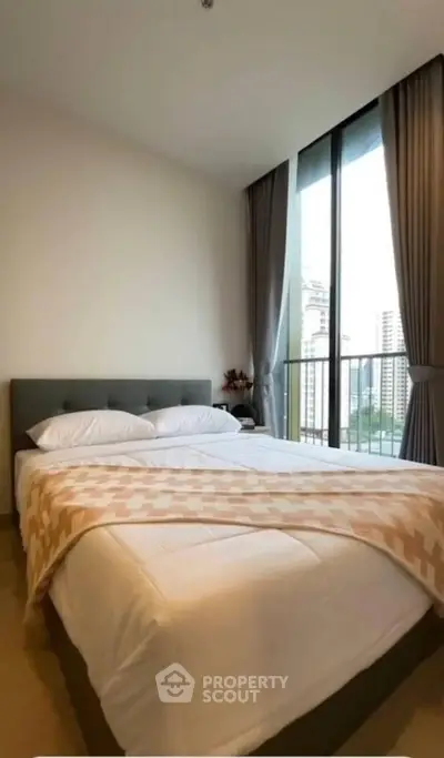 Cozy bedroom with large window offering city view, modern decor and comfortable bedding.
