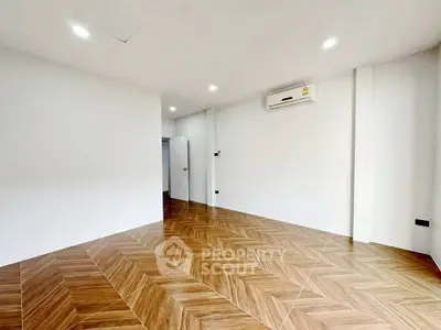 Spacious empty room with elegant wooden flooring and modern air conditioning unit.