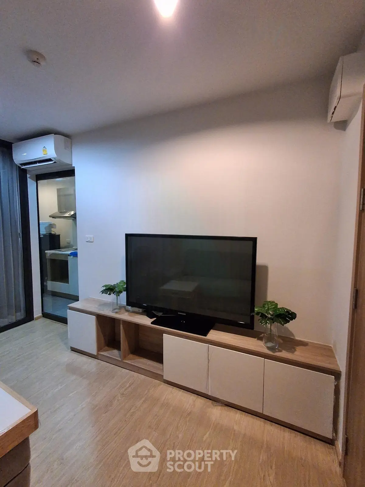 Modern living room with sleek TV stand and air conditioning, featuring a glimpse into a stylish kitchen.