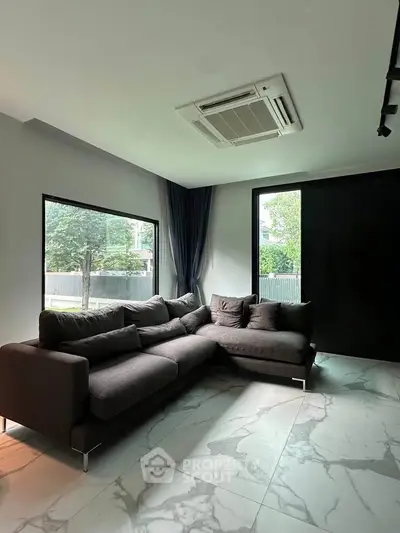 Modern living room with large windows and stylish dark sofa, featuring elegant marble flooring.