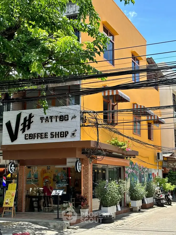 Vibrant yellow building with tattoo and coffee shop, lush greenery, and street view.