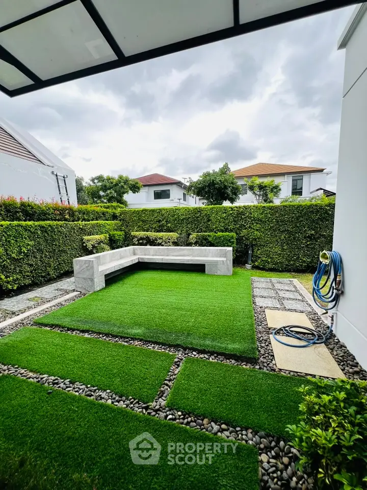 Charming backyard with lush green lawn and modern stone seating area, perfect for outdoor relaxation.