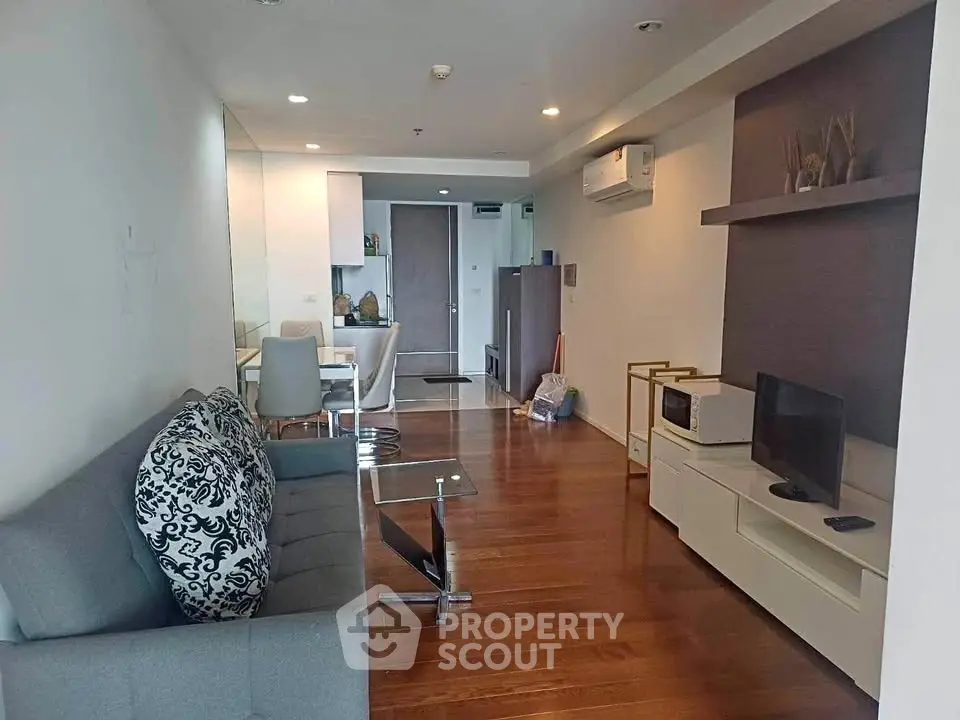 Modern living room with wooden flooring, stylish furniture, and open kitchen layout in a cozy apartment.