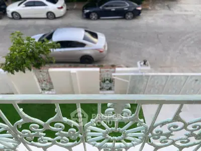 Charming balcony view overlooking a quiet street with parked cars and lush greenery.