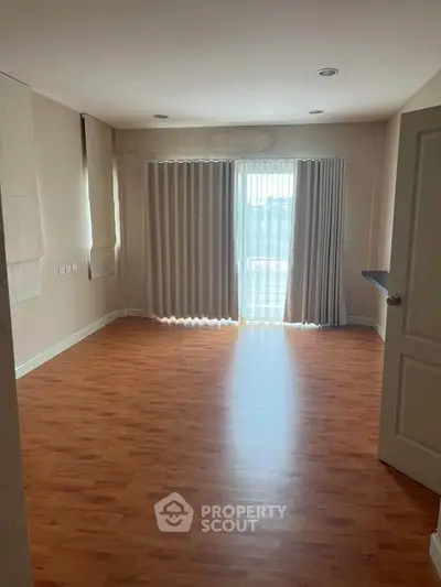 Spacious empty room with wooden flooring and large windows with curtains, ideal for customization.