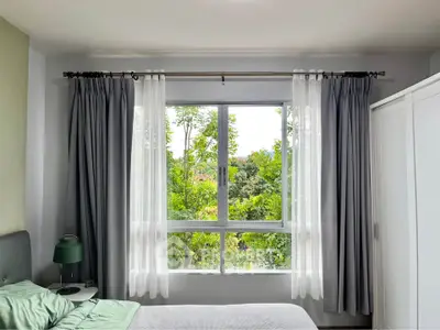 Bright bedroom with large window and lush green view, featuring modern decor and ample natural light.