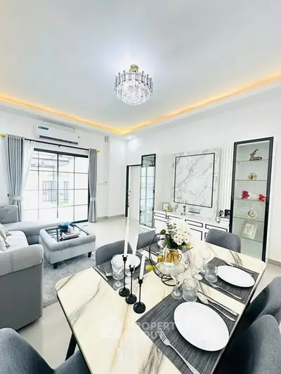 Elegant living room with modern decor and dining area, featuring a chandelier and large windows.
