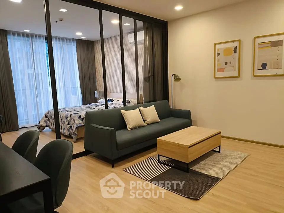 Modern living room with stylish decor and glass partition leading to a cozy bedroom.
