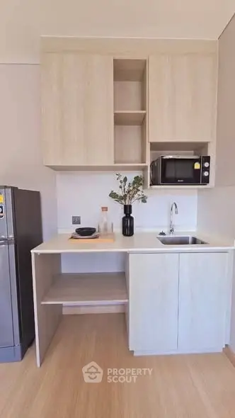 Modern compact kitchen with light wood cabinets, microwave, and stainless steel fridge.