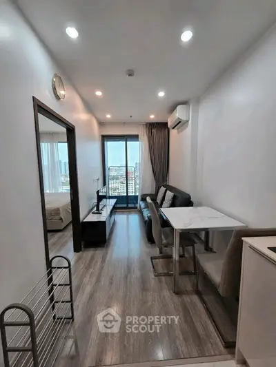 Modern apartment interior with open living room and dining area, featuring sleek furniture and city view balcony.