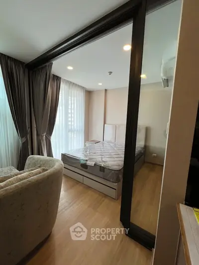 Modern bedroom with large windows and cozy seating area, featuring elegant curtains and wooden flooring.