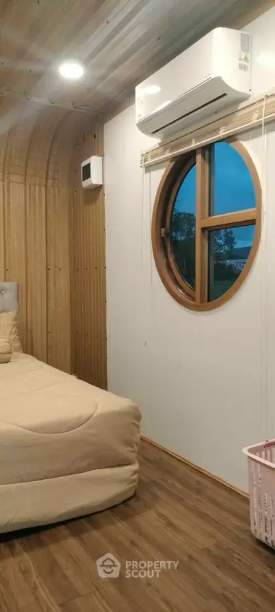 Cozy bedroom with round window and air conditioning in modern wooden cabin.