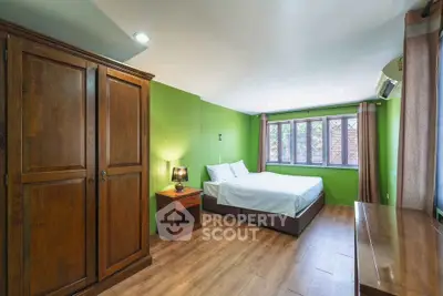 Spacious bedroom with wooden furniture and green walls, featuring a cozy bed and ample natural light.