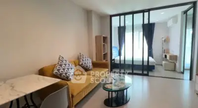 Modern living room with glass partition leading to bedroom, featuring stylish furniture and natural light.