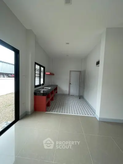 Modern kitchen with red cabinetry and open layout, featuring sleek tile flooring and ample natural light.