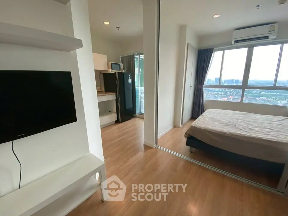 Modern apartment interior with bedroom and living area, featuring large windows and wooden flooring.