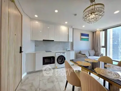Modern open-plan kitchen and living area with elegant chandelier and natural light.
