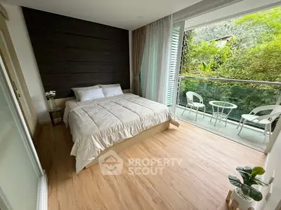 Spacious bedroom with large windows and balcony overlooking lush greenery, featuring modern decor and wooden flooring.