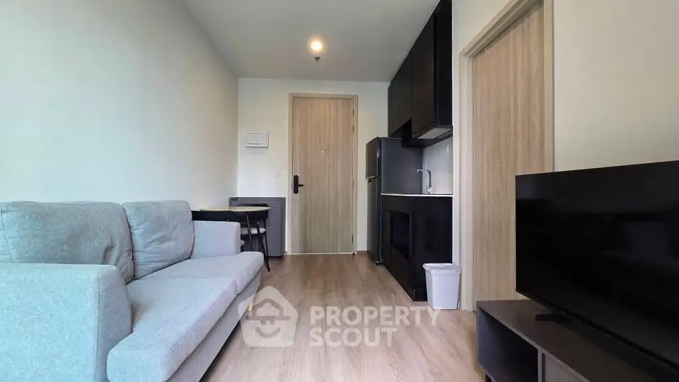 Modern living room with sleek black kitchen and cozy gray sofa in a stylish apartment.