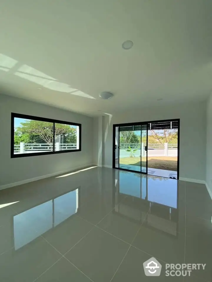 Spacious and sunlit living room with gleaming floor tiles, large windows, and glass doors leading to an inviting outdoor area, perfect for modern living.