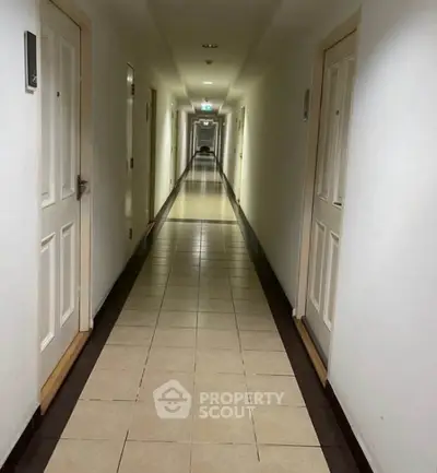 Long corridor in a residential building with tiled flooring and multiple doors.