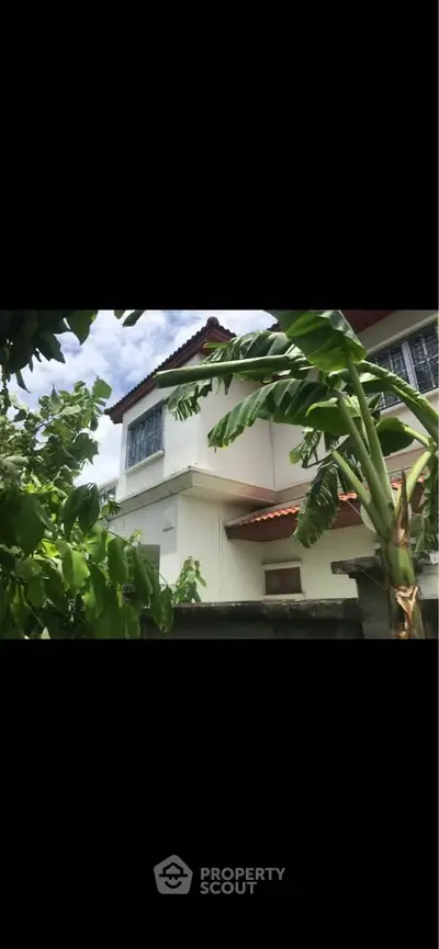 Charming two-story house with lush greenery and tropical banana trees in the foreground.