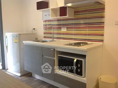 Modern kitchen with sleek cabinetry and colorful backsplash, featuring a compact fridge and microwave.