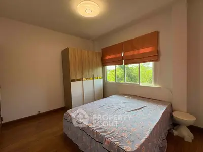 Cozy bedroom with large window and wooden wardrobe, perfect for relaxation.