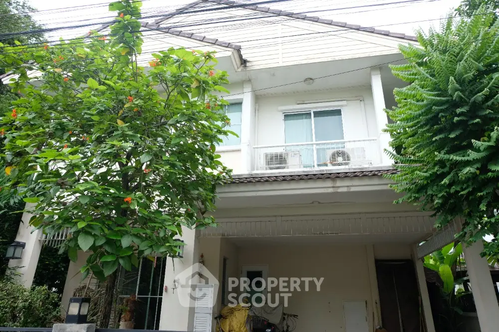 Charming two-story house with lush greenery and spacious carport, perfect for family living.