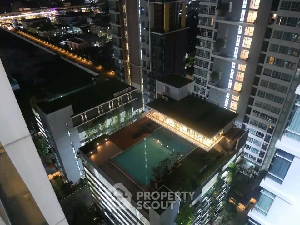 Stunning aerial view of modern high-rise buildings with illuminated rooftop pool at night.