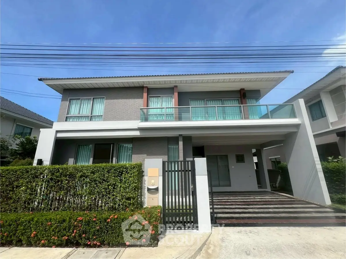 Modern two-story house with large windows and manicured hedges under a clear blue sky.