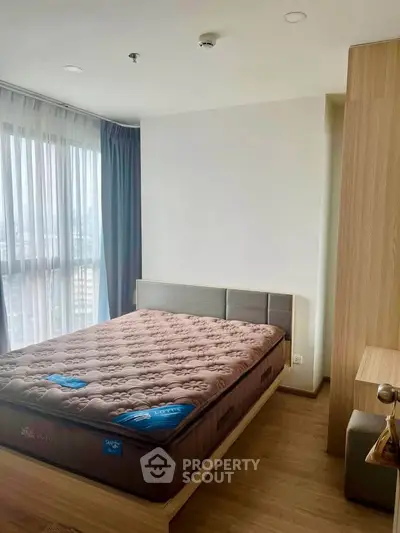 Modern bedroom with large window and stylish furnishings in high-rise apartment.