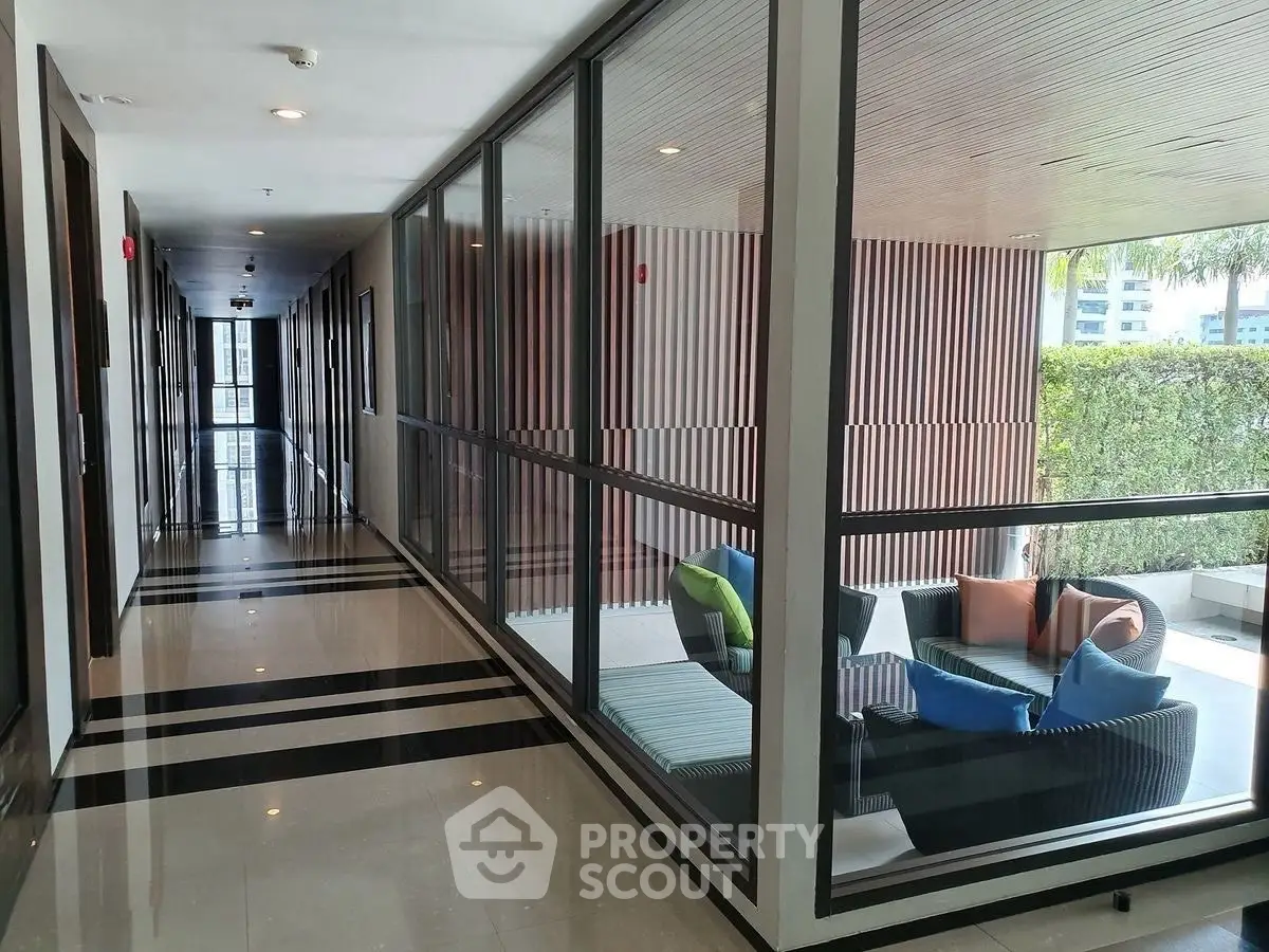 Modern corridor with glass walls and outdoor seating area in luxury building.