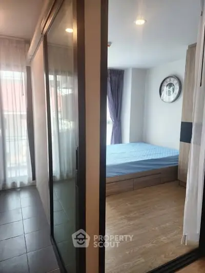 Modern bedroom with wooden flooring and large window, featuring a stylish clock and ample natural light.