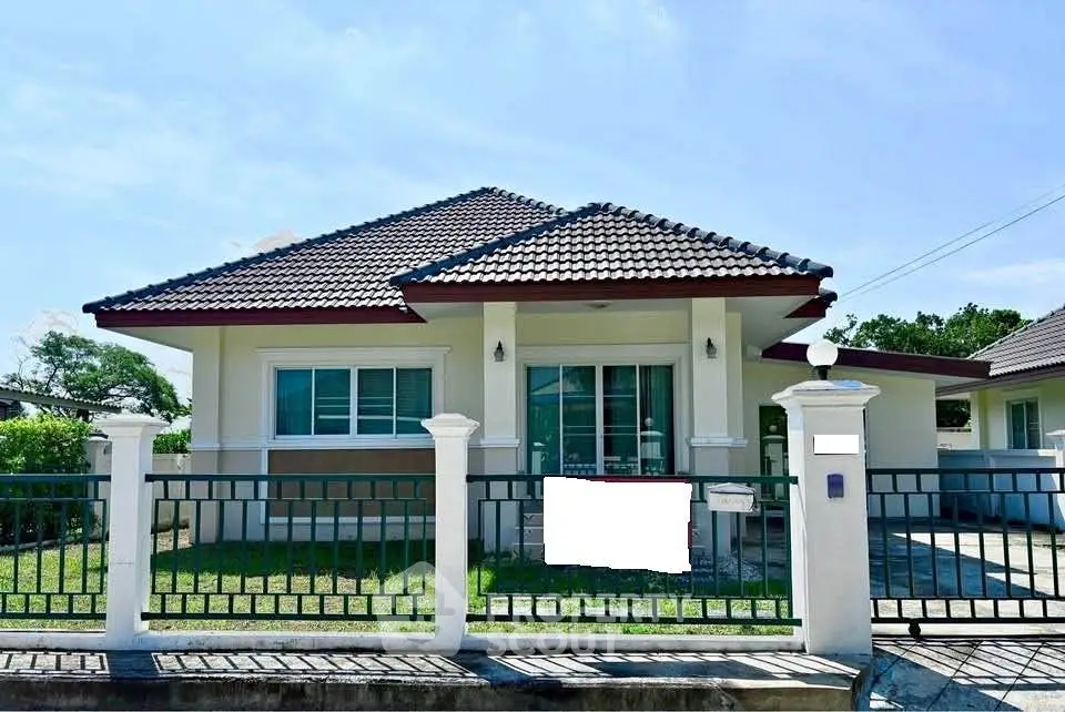Charming single-story house with tiled roof and fenced yard under clear blue sky.