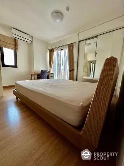 Spacious bedroom with modern design and natural light, featuring wooden flooring and mirrored wardrobe.