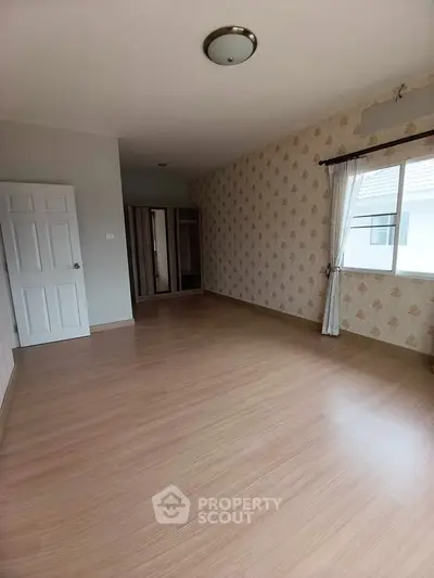 Spacious empty bedroom with wooden flooring and large window
