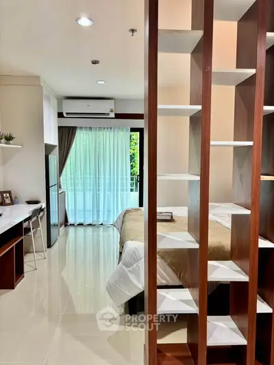 Modern studio apartment with open layout and balcony view, featuring sleek shelving and cozy decor.