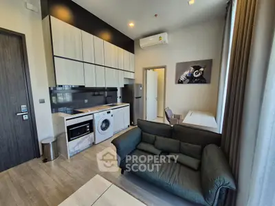 Modern living room with integrated kitchen featuring washing machine and sleek cabinetry.
