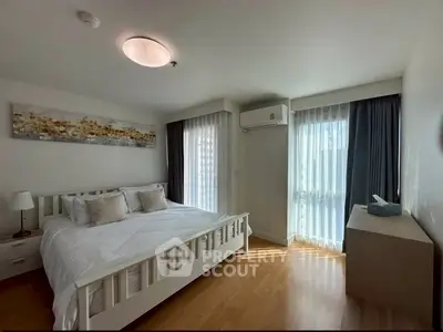 Spacious bedroom with natural light, modern decor, and wooden flooring in a stylish apartment.