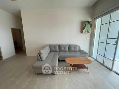 Spacious living room with modern gray sectional sofa and wooden coffee table, featuring large windows for natural light.