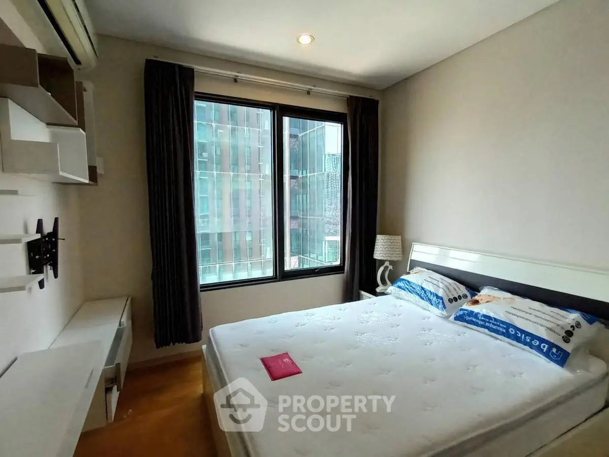 Modern bedroom with large window and city view, featuring a comfortable bed and stylish decor.
