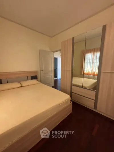 Cozy bedroom with wooden flooring and mirrored wardrobe, perfect for a restful retreat.