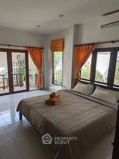 Spacious bedroom with large windows and garden view, featuring elegant curtains and cozy bedding.