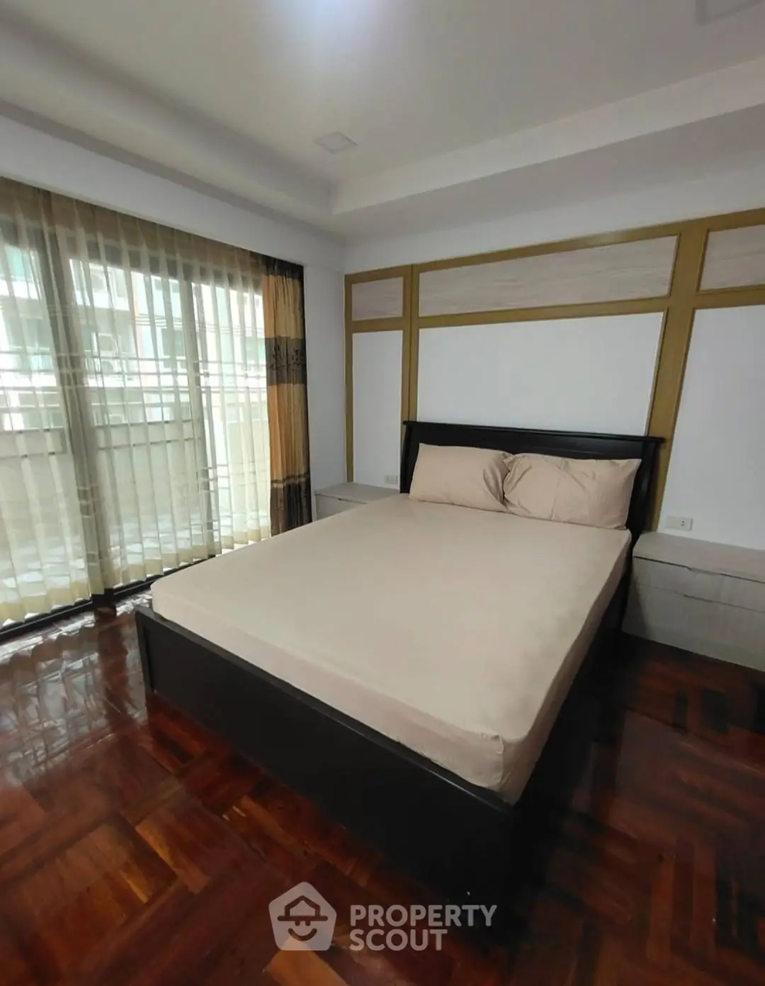 Spacious bedroom with elegant wooden flooring and large window for natural light.
