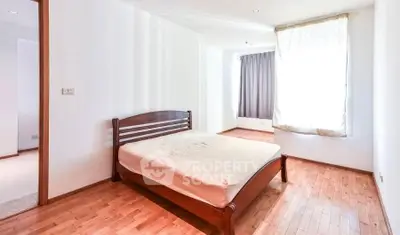 Spacious bedroom with wooden flooring and large window for natural light.