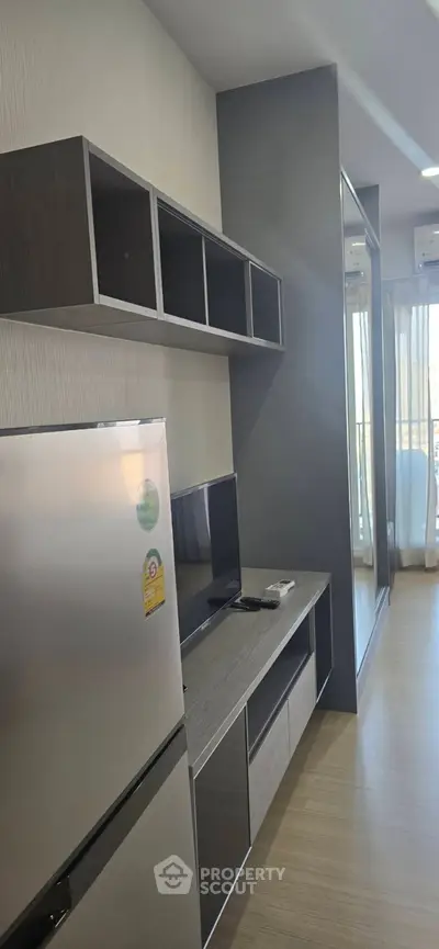 Modern apartment interior with sleek kitchen and living area, featuring stainless steel fridge and wall-mounted TV.