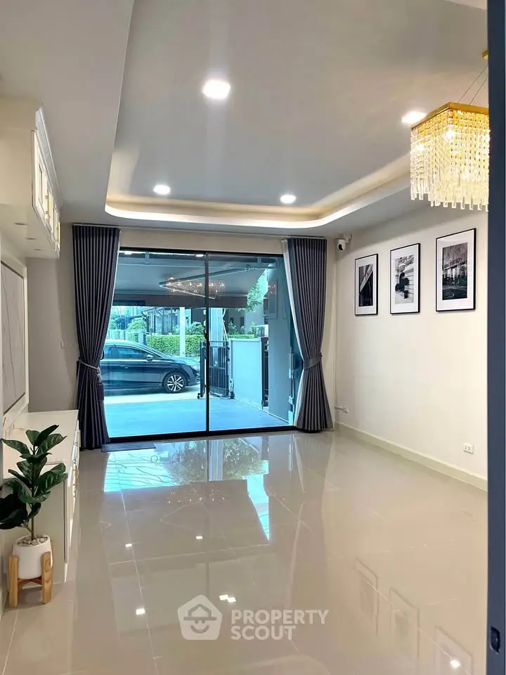 Spacious living room with elegant chandelier and large glass doors leading to a garden view.
