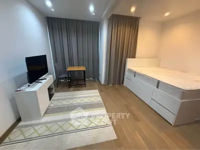 Modern minimalist bedroom with wooden flooring, TV setup, and cozy bed.