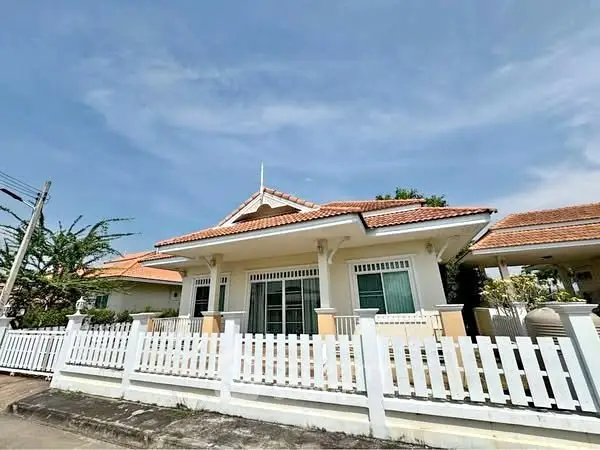 Charming single-story home with white picket fence and red-tiled roof under clear blue sky.